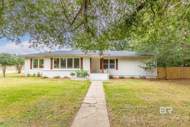ranch-style home featuring a shingled roof, a front yard, fence, and board and batten siding