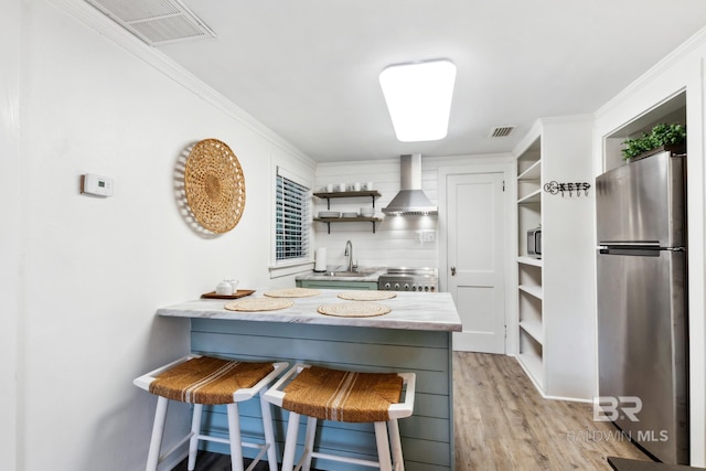 kitchen with ornamental molding, wall chimney exhaust hood, a sink, open shelves, and freestanding refrigerator