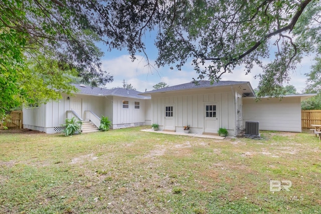 back of house with fence, board and batten siding, entry steps, central AC unit, and a yard