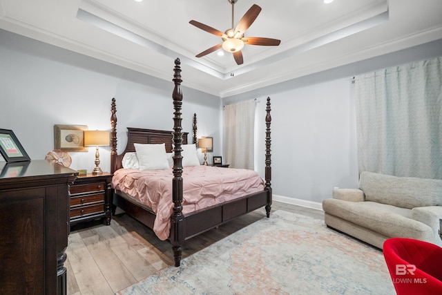 bedroom with light wood-type flooring, a raised ceiling, ceiling fan, and ornamental molding