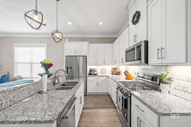 kitchen featuring appliances with stainless steel finishes, ornamental molding, a kitchen island with sink, wood-type flooring, and white cabinetry