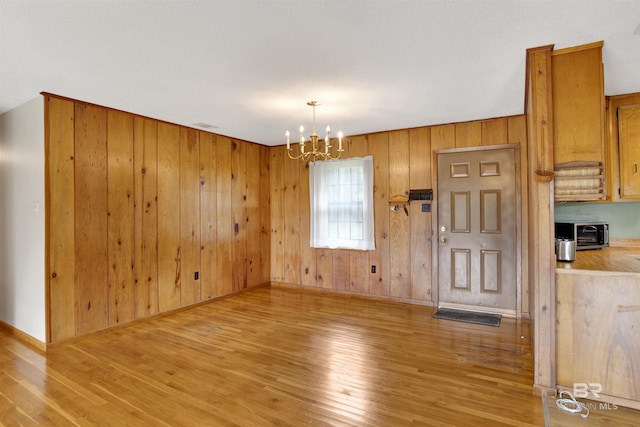 interior space featuring a chandelier, baseboards, light wood-style flooring, and wooden walls