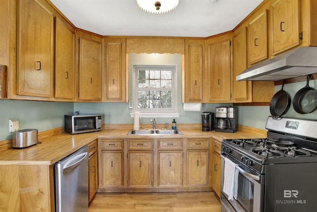 kitchen featuring light wood finished floors, light countertops, appliances with stainless steel finishes, a sink, and under cabinet range hood