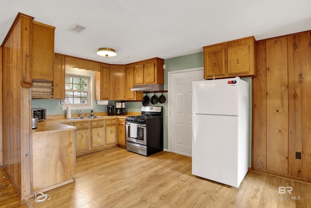 kitchen with light wood finished floors, light countertops, visible vents, freestanding refrigerator, and stainless steel gas range