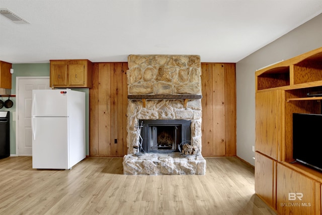 kitchen with brown cabinets, visible vents, light wood-style flooring, freestanding refrigerator, and a stone fireplace