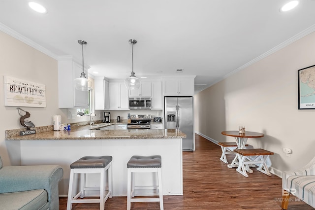 kitchen featuring white cabinetry, wood-type flooring, pendant lighting, sink, and appliances with stainless steel finishes