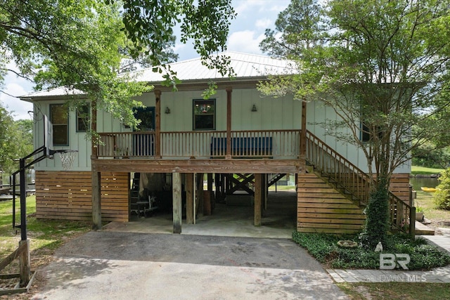 raised beach house with covered porch, a carport, stairs, and aphalt driveway