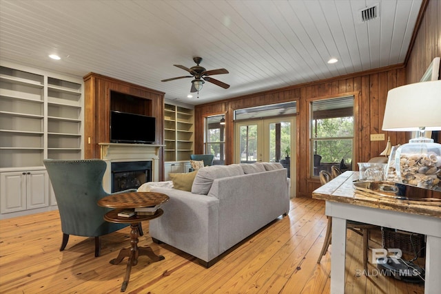 living area with wooden walls, a ceiling fan, a fireplace, and french doors