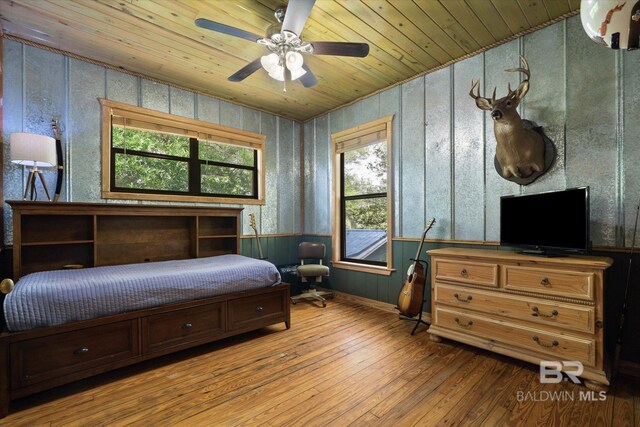 bedroom featuring wood walls, wainscoting, hardwood / wood-style flooring, wooden ceiling, and a ceiling fan