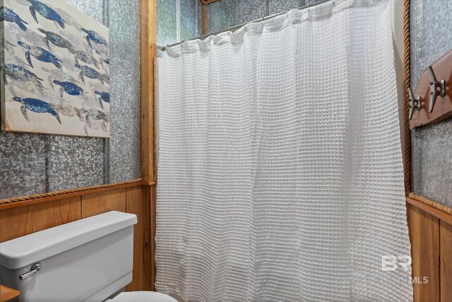 full bathroom featuring wooden walls and toilet