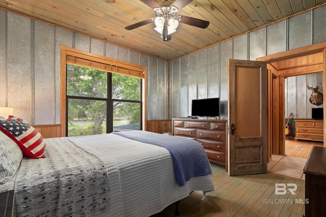 bedroom featuring wood walls, wainscoting, hardwood / wood-style floors, wood ceiling, and a ceiling fan