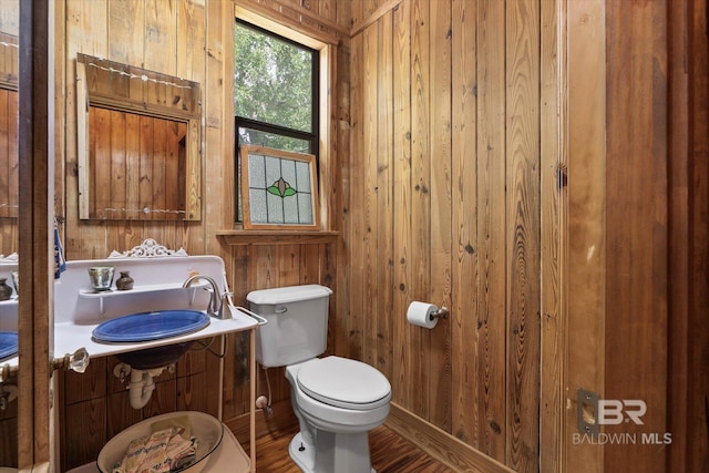half bathroom with vanity, toilet, wood walls, and wood finished floors