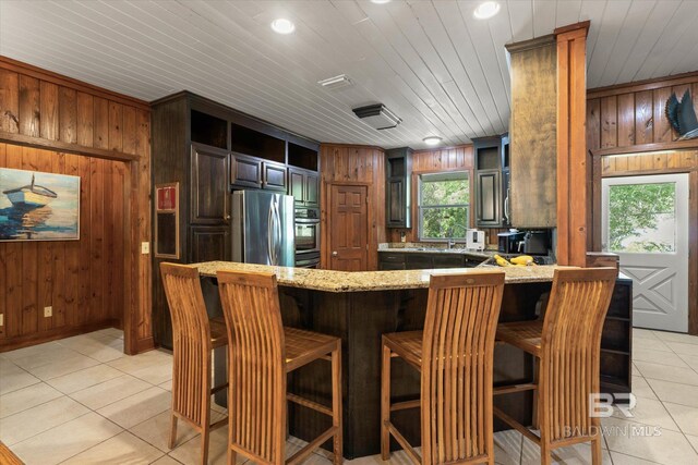 kitchen featuring wooden walls, appliances with stainless steel finishes, light stone counters, and light tile patterned flooring