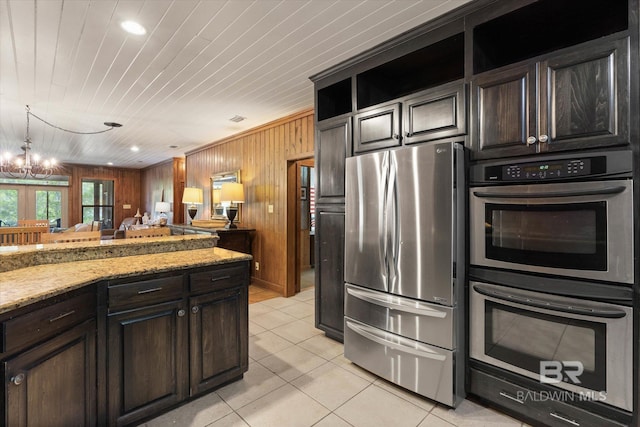 kitchen featuring wooden walls, light tile patterned flooring, light stone countertops, a notable chandelier, and stainless steel appliances