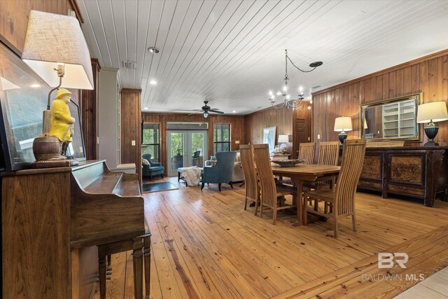 dining space featuring visible vents, wooden walls, wood ceiling, light wood-style flooring, and ceiling fan with notable chandelier