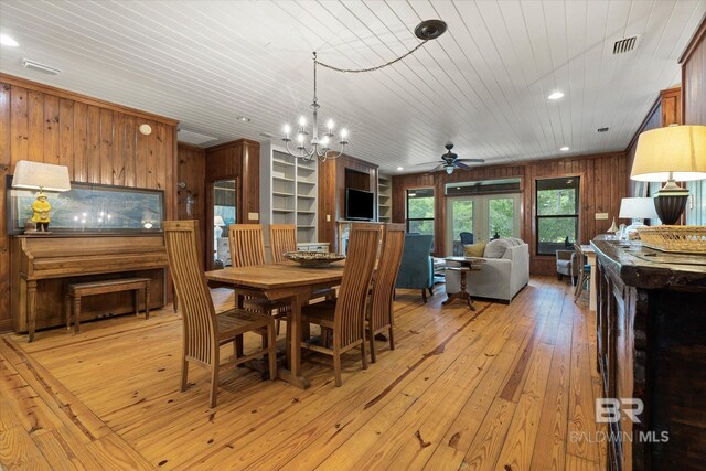 dining space with visible vents, wood walls, wooden ceiling, light wood finished floors, and ceiling fan with notable chandelier