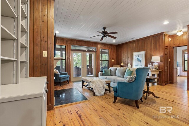 living area with french doors, wood walls, ceiling fan, and a healthy amount of sunlight