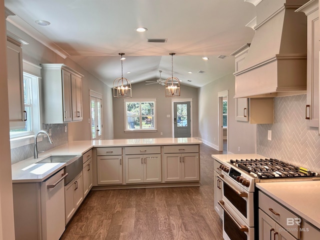 kitchen with kitchen peninsula, a chandelier, appliances with stainless steel finishes, custom range hood, and vaulted ceiling