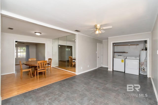 living room with dark wood-type flooring, gas water heater, ceiling fan, washer and clothes dryer, and ornamental molding