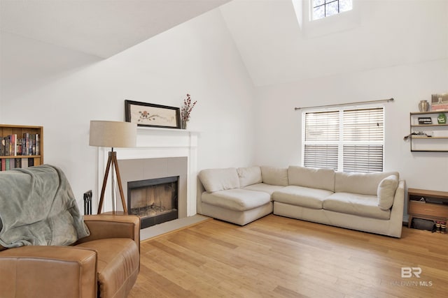 living room featuring hardwood / wood-style flooring, high vaulted ceiling, and a tile fireplace