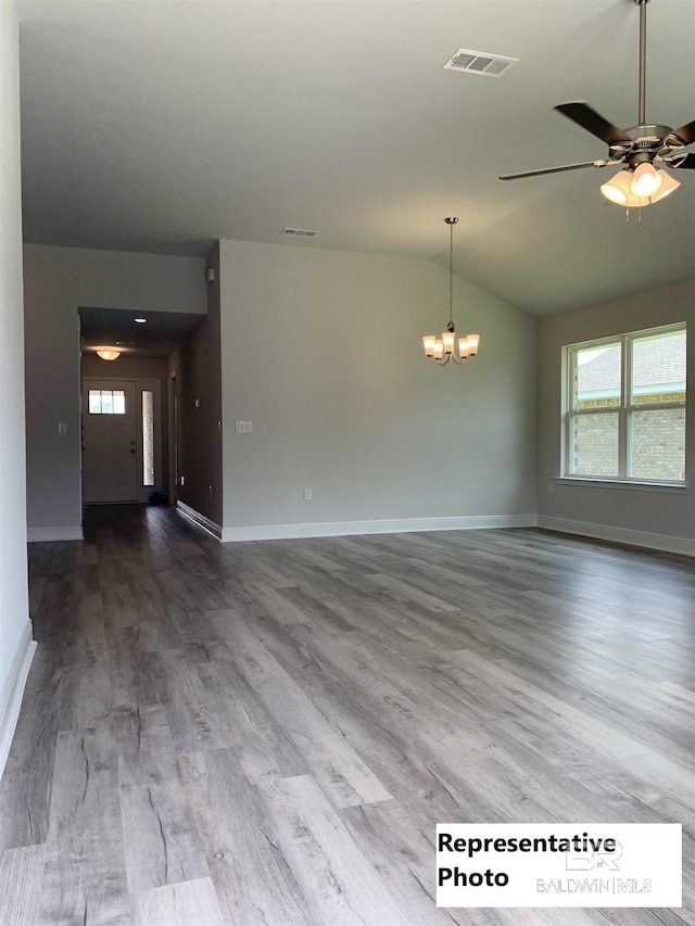 spare room featuring lofted ceiling, wood-type flooring, and ceiling fan with notable chandelier