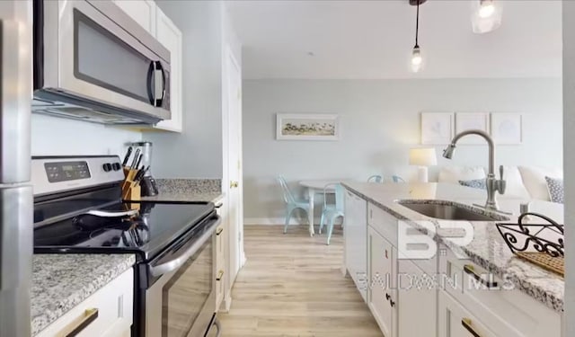 572 E Beach Blvd Unit 318, Gulf Shores, AL 36542 - kitchen with appliances with stainless steel finishes, a sink, light wood-style floors, white cabinets, and light stone countertops