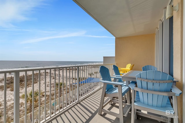 balcony with a beach view, outdoor dining area, and a water view