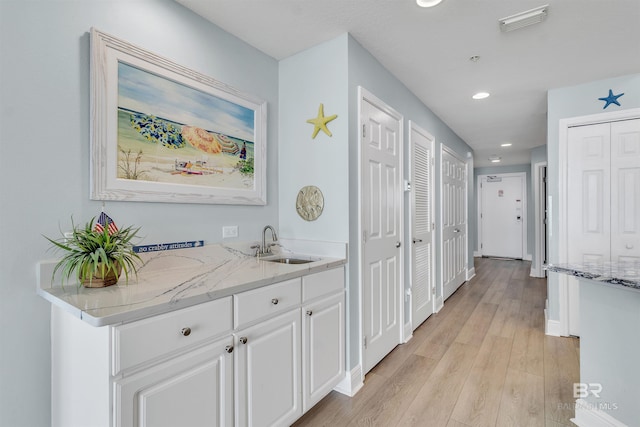 corridor with baseboards, visible vents, recessed lighting, a sink, and light wood-type flooring