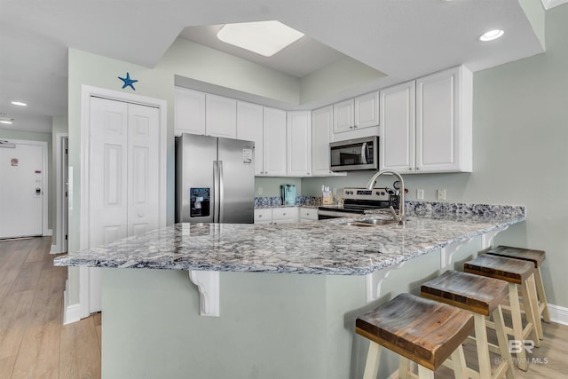 kitchen with light stone counters, appliances with stainless steel finishes, a peninsula, and light wood finished floors