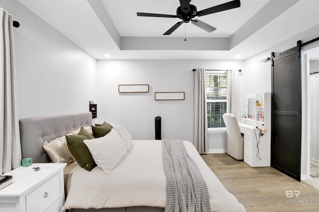 bedroom featuring a barn door, light wood-style floors, recessed lighting, a raised ceiling, and ceiling fan