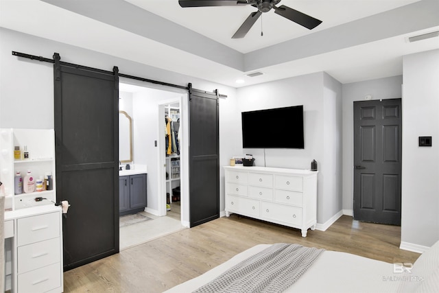 bedroom featuring a barn door, light wood-style flooring, a walk in closet, baseboards, and ensuite bath