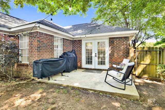rear view of property with french doors, brick siding, roof with shingles, fence, and a patio