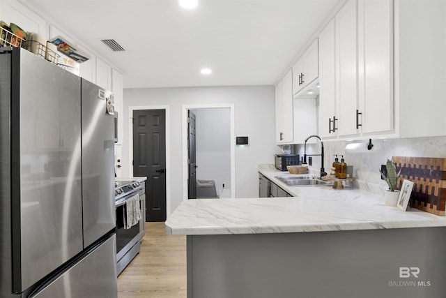 kitchen featuring stainless steel appliances, a sink, light wood finished floors, white cabinets, and light stone countertops