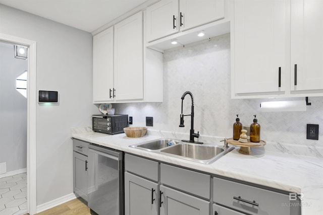 kitchen with a sink, gray cabinetry, stainless steel dishwasher, backsplash, and baseboards