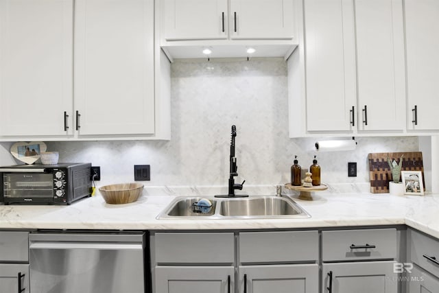 kitchen featuring dishwasher, a sink, tasteful backsplash, and white cabinetry