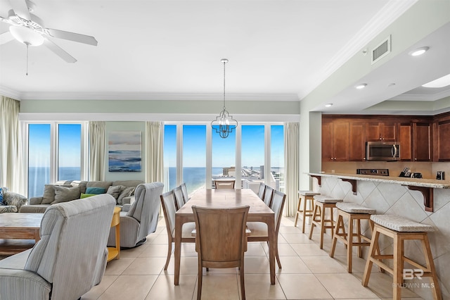 dining area featuring visible vents, a water view, ornamental molding, light tile patterned floors, and ceiling fan with notable chandelier