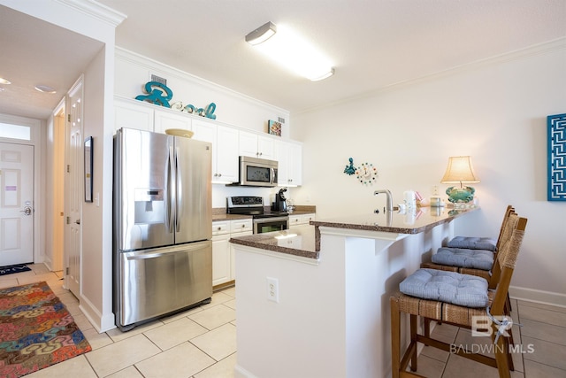 kitchen featuring ornamental molding, appliances with stainless steel finishes, white cabinets, and a kitchen bar