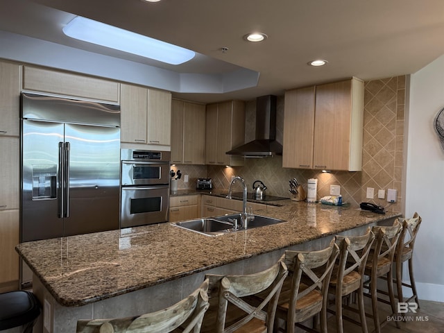 28105 Perdido Beach Blvd Unit C211, Orange Beach, AL 36561 - kitchen featuring backsplash, wall chimney exhaust hood, a breakfast bar area, stainless steel appliances, and a sink
