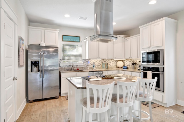 kitchen featuring white cabinets, sink, light wood-type flooring, island range hood, and stainless steel appliances