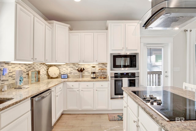 kitchen featuring light stone countertops, tasteful backsplash, white cabinets, exhaust hood, and appliances with stainless steel finishes