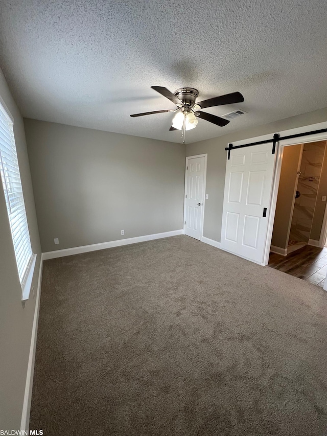 15082 County Road 93, Lillian, AL 36549 - unfurnished bedroom featuring ceiling fan, a barn door, carpet floors, and a textured ceiling