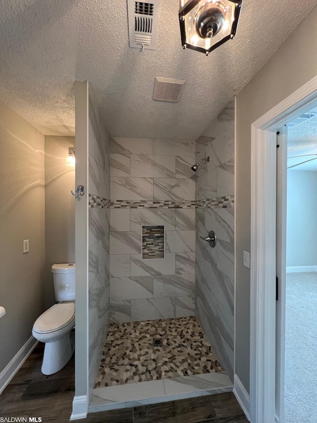 15082 County Road 93, Lillian, AL 36549 - bathroom featuring a textured ceiling, toilet, a tile shower, and hardwood / wood-style floors