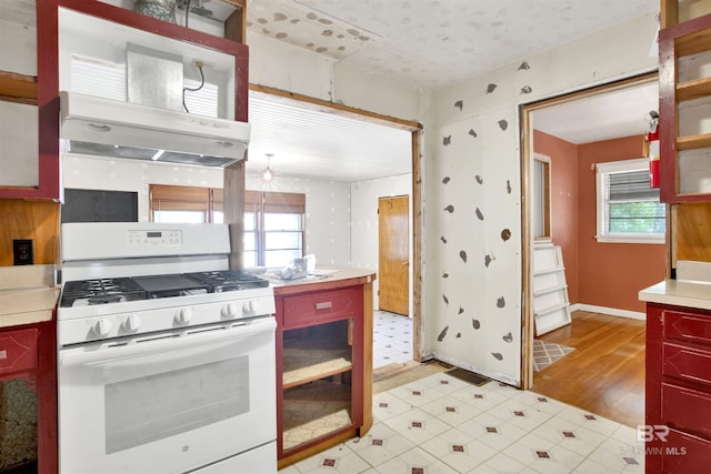 kitchen with light countertops, white gas range, range hood, baseboards, and light floors