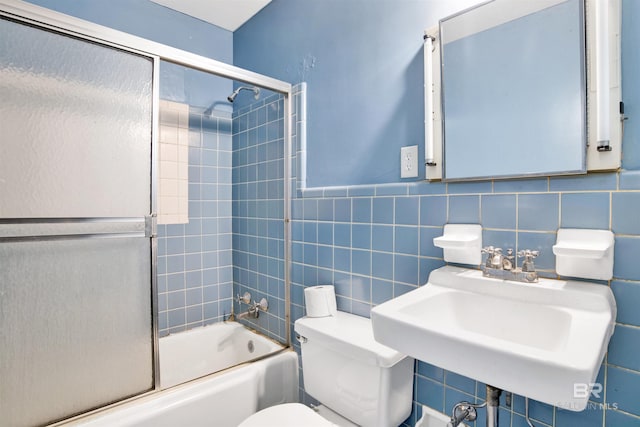 bathroom featuring tile walls, shower / bath combination with glass door, toilet, and a sink