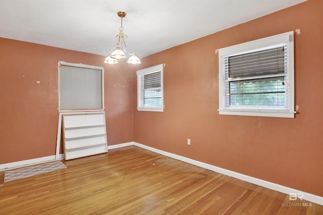 empty room with baseboards, a chandelier, and light wood-type flooring