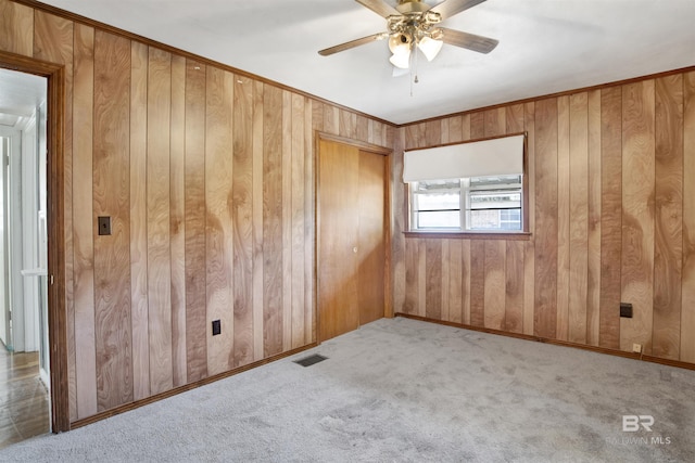 carpeted spare room featuring baseboards, visible vents, a ceiling fan, and wood walls