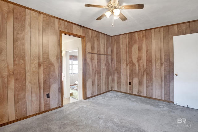 carpeted spare room with ceiling fan, wood walls, and crown molding