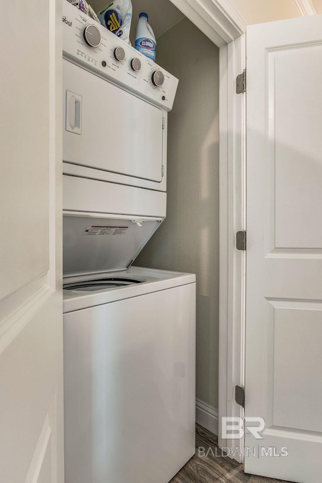 clothes washing area featuring stacked washer and dryer and dark hardwood / wood-style flooring