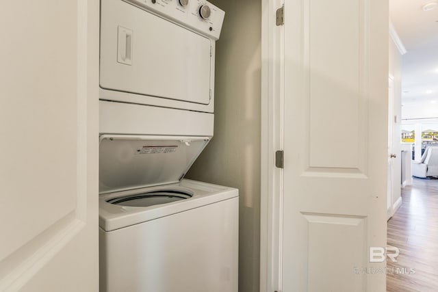 clothes washing area with stacked washer / drying machine, crown molding, and light hardwood / wood-style floors