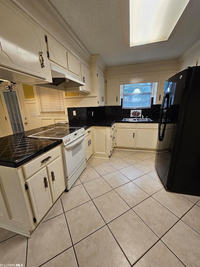 kitchen with tile counters, white cabinetry, black fridge, and white range